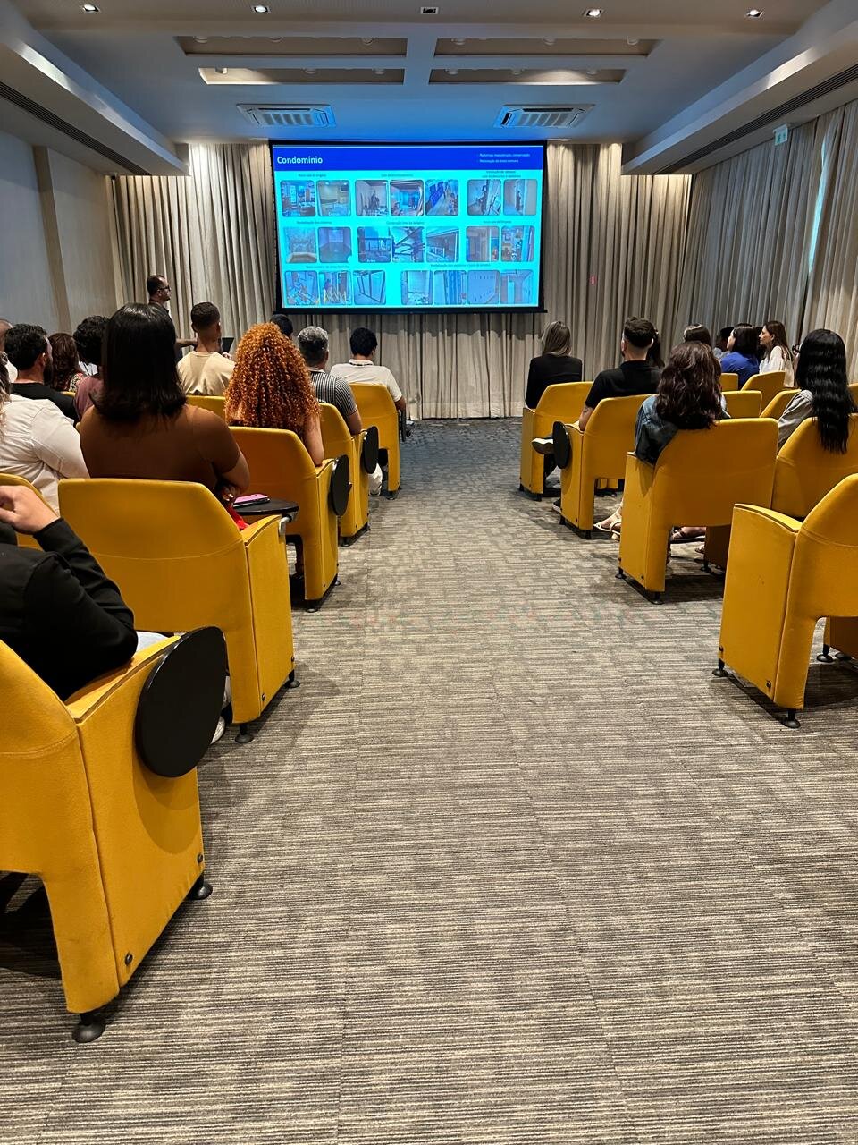 Treinamento em auditório com equipe assistindo apresentação sobre gestão de condomínio